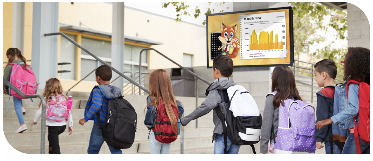 School children in a line arriving at school. Screen in the background displaying the amount of solar energy the school produces in a month.