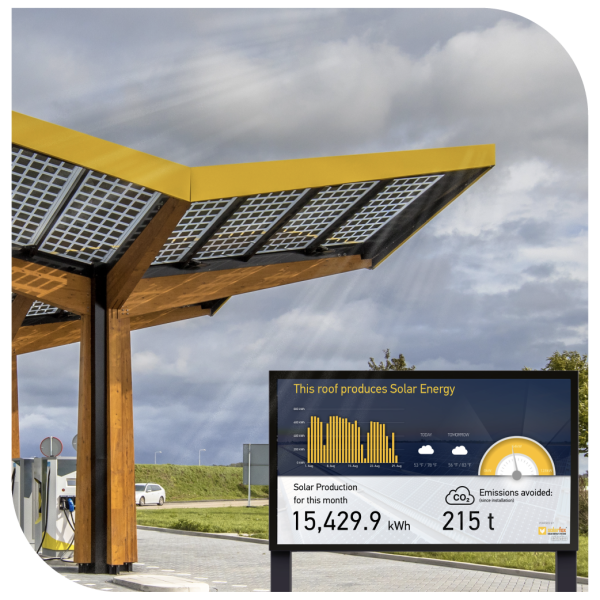 A solar panelled roof outside with car charging ports. With a screen displaying the amount of solar energy the roof produces
