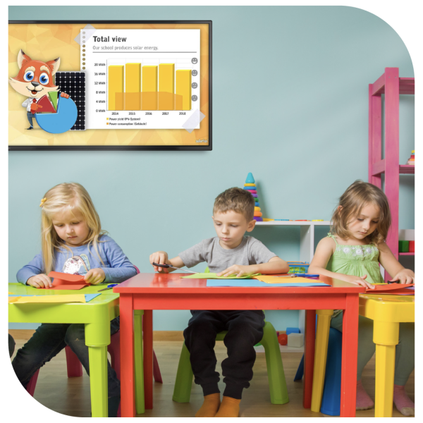 3 school children sitting at their desks doing crafts with a screen behind them displaying the amount of solar energy the school produces